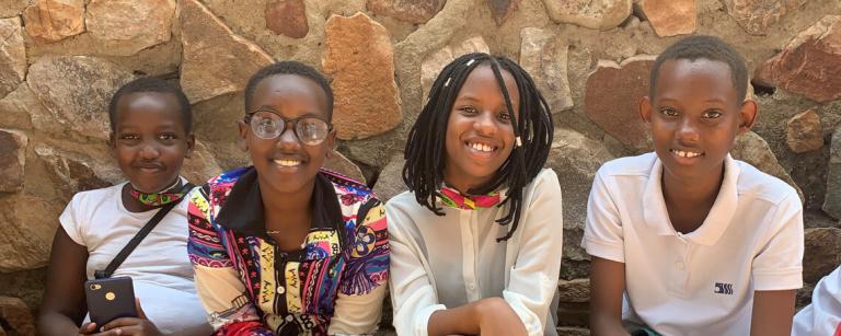 four children sat on a bench in front of a wall relaxed and smiling