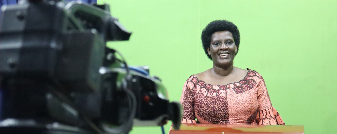 a woman stands at a lectern in front of a greenscree, a camera is focused on her