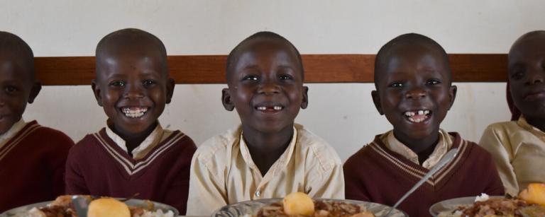 School Children sit smiling waiting to eat plates of food
