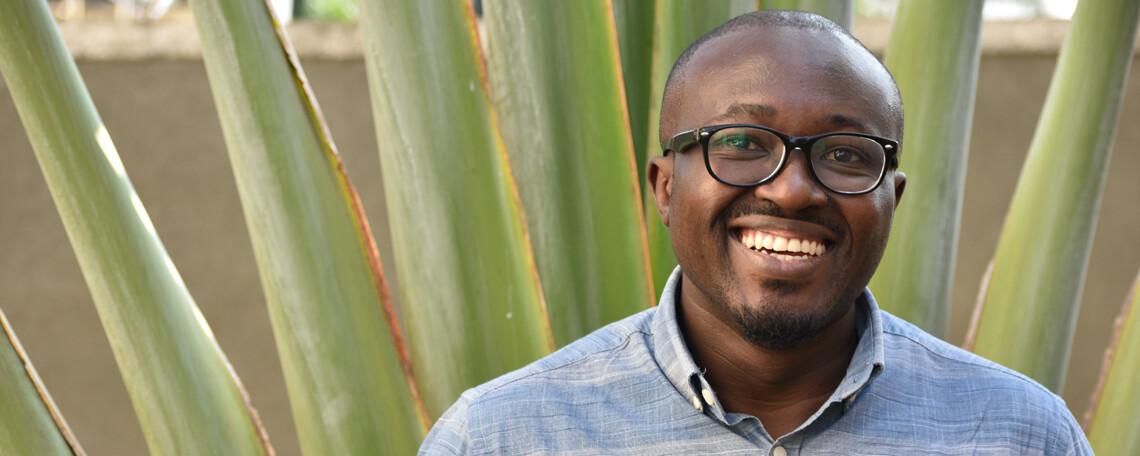 Audry Masabo smiling in front of a large plant