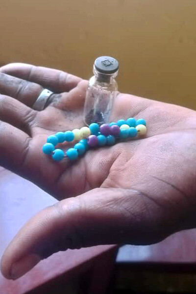 A hand holding a small jar with some ash, and a bracelet of beads.